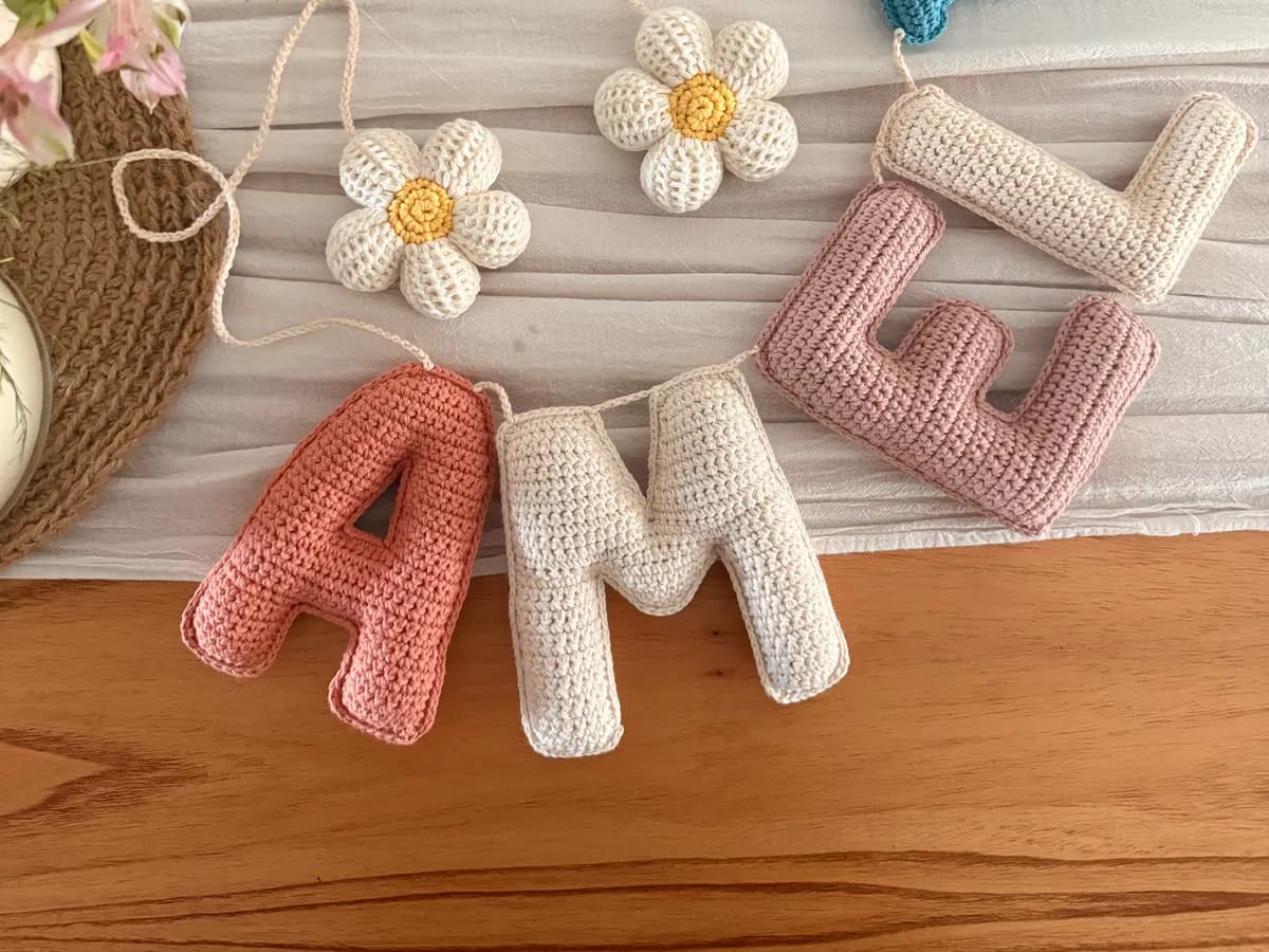 Cartel de letras tejidas al crochet, con flores y un colgante